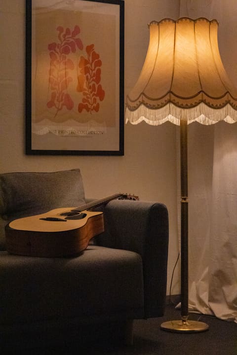 Akustikgitarre auf der Sofalehne neben der Fransen-Stehlampe.